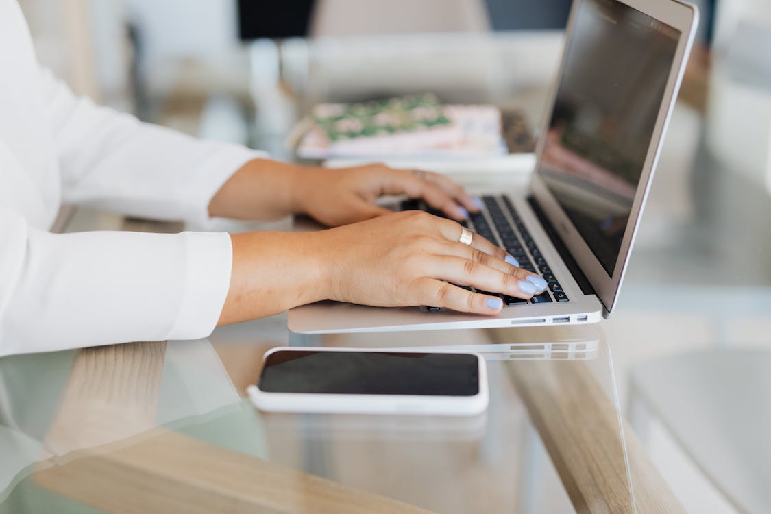 Person typing on a laptop with a smartphone on the desk