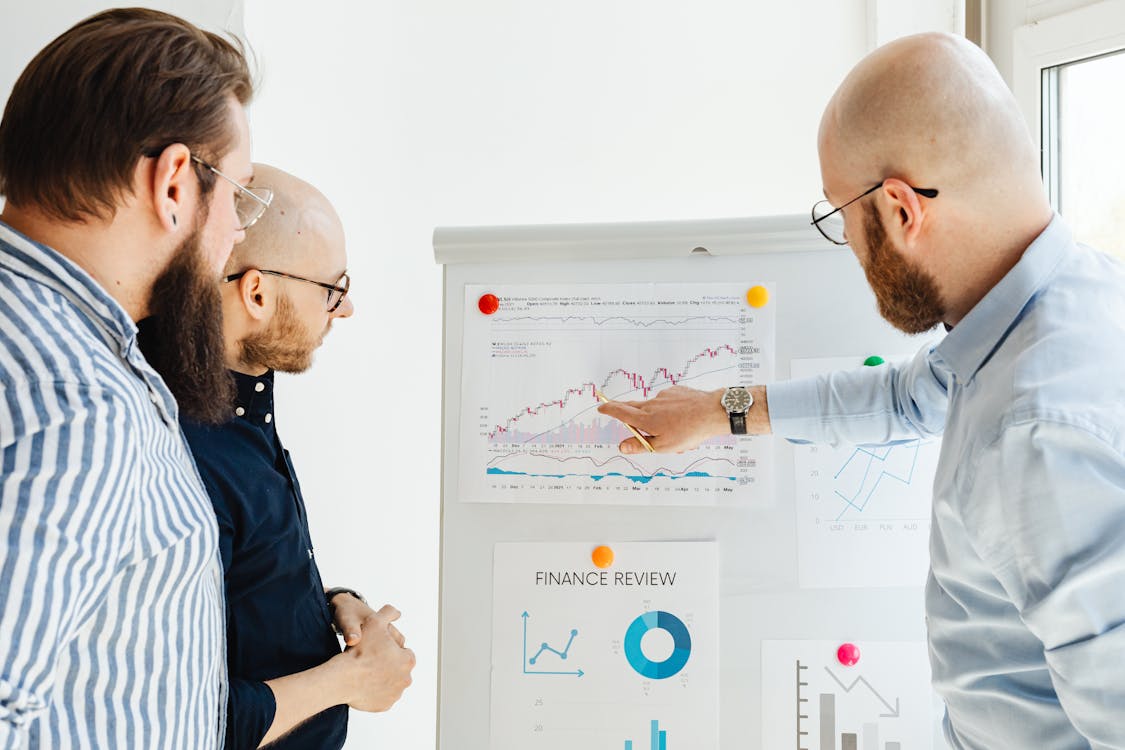 Three professionals discussing a finance review with charts on a whiteboard